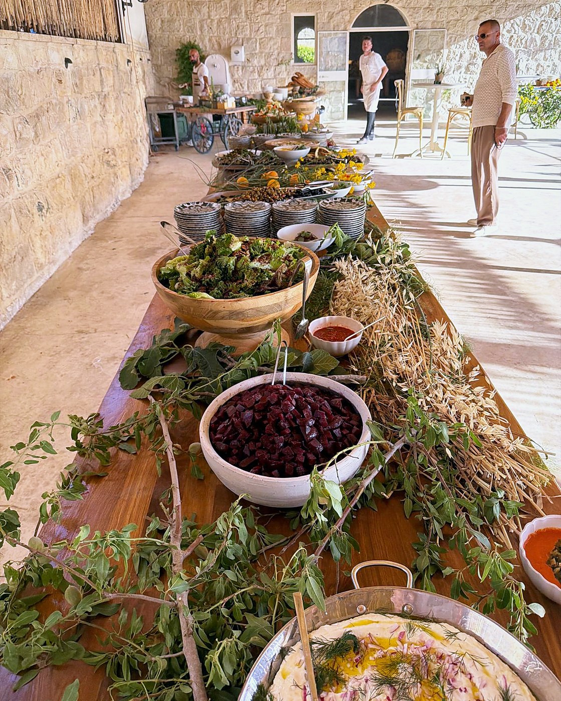 A long grazing table dressed with herbs and olive branches in a stone hall