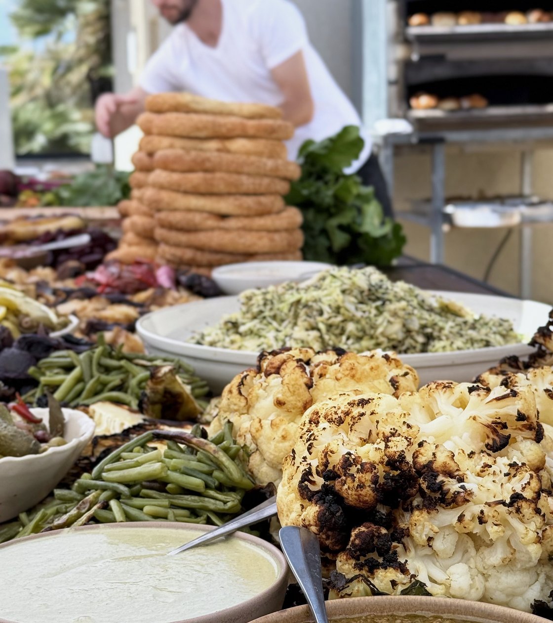 Sesame bread stacked high beside a wood-fired oven at an outdoor feast